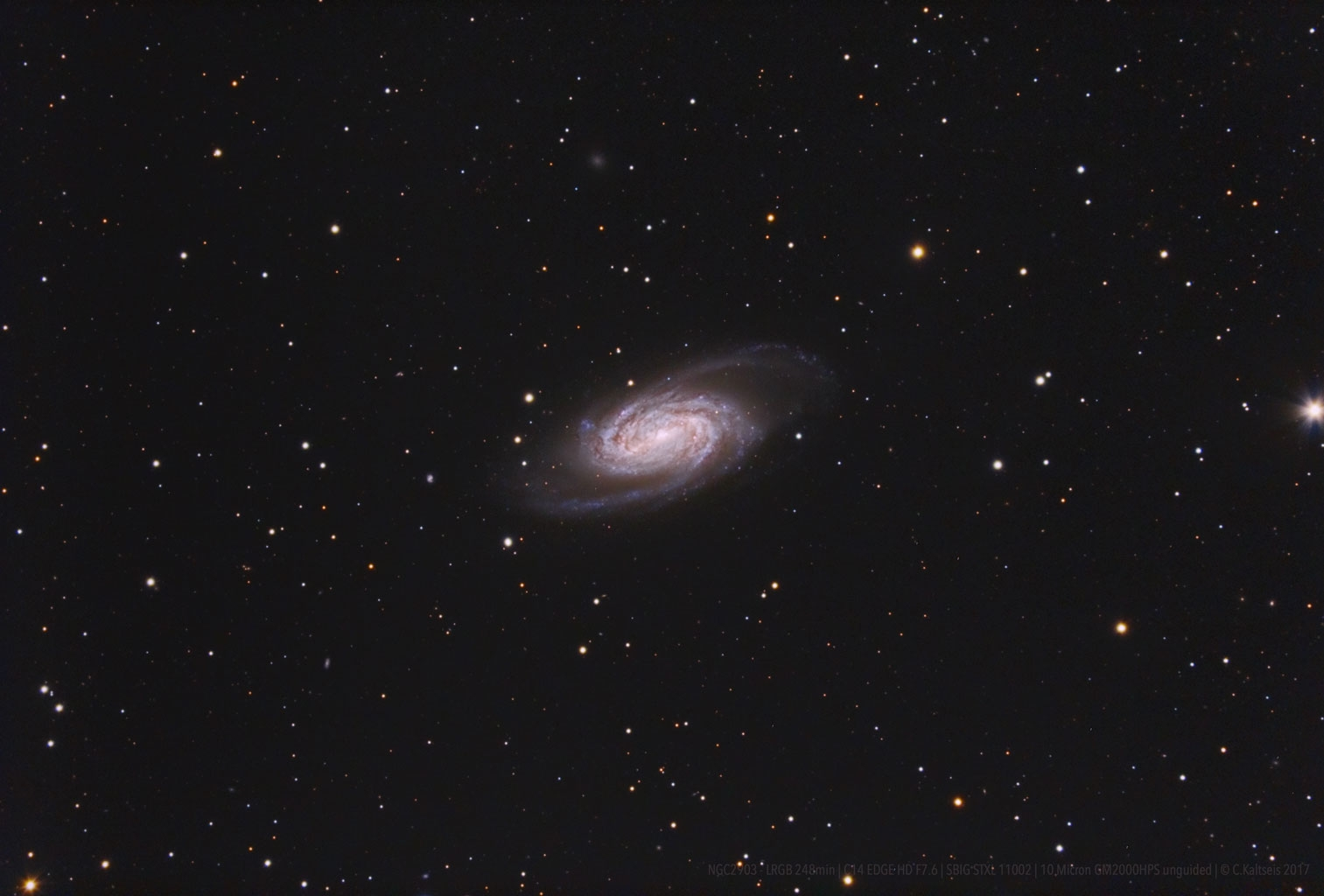 Eine Spiralgalaxie in der Mitte des Bildes, umgeben von zahlreichen Sternen in einem dunklen Himmel.