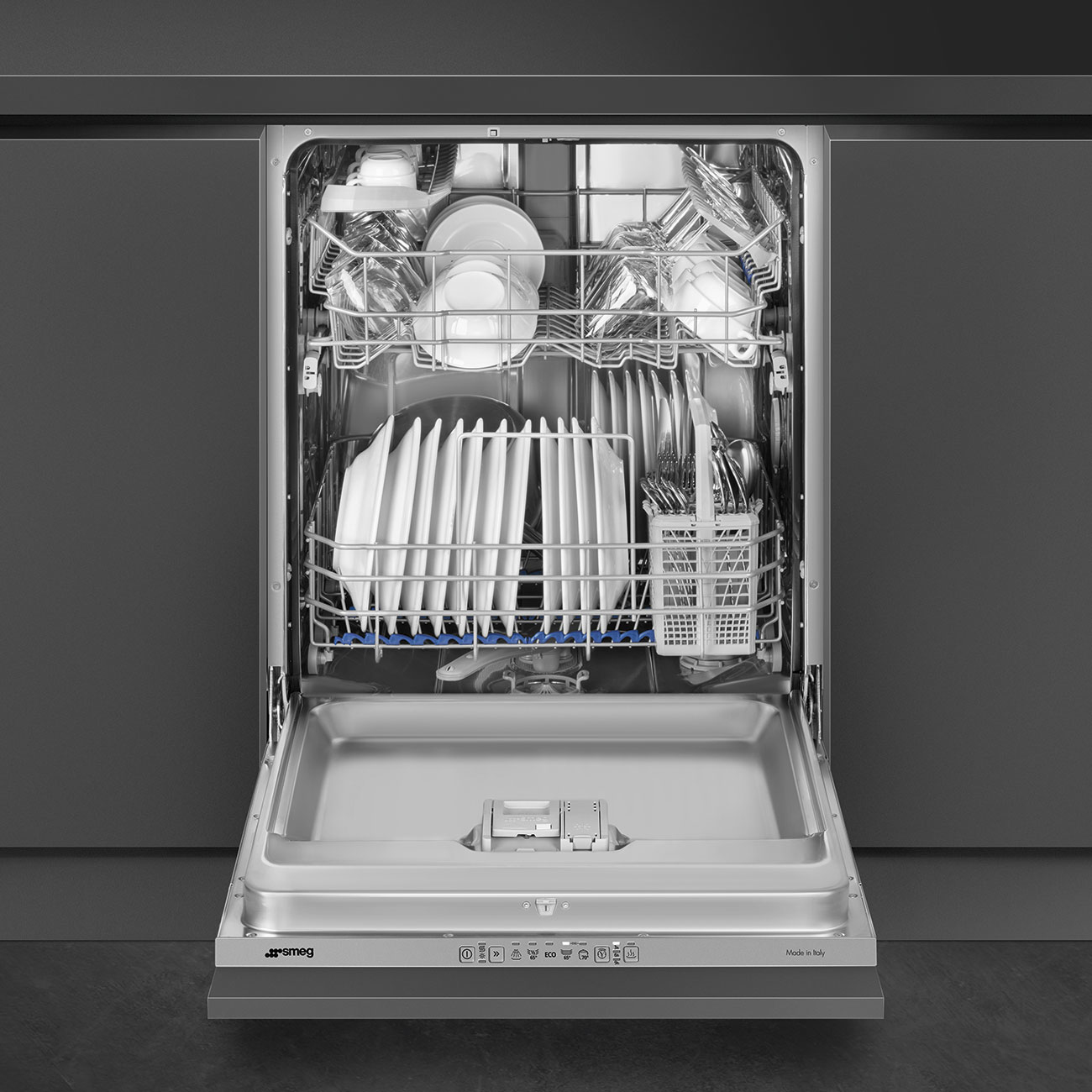 Lavastoviglie SMEG aperta, interno in acciaio inox, con piatti, posate e bicchieri. Inserita in mobili scuri.