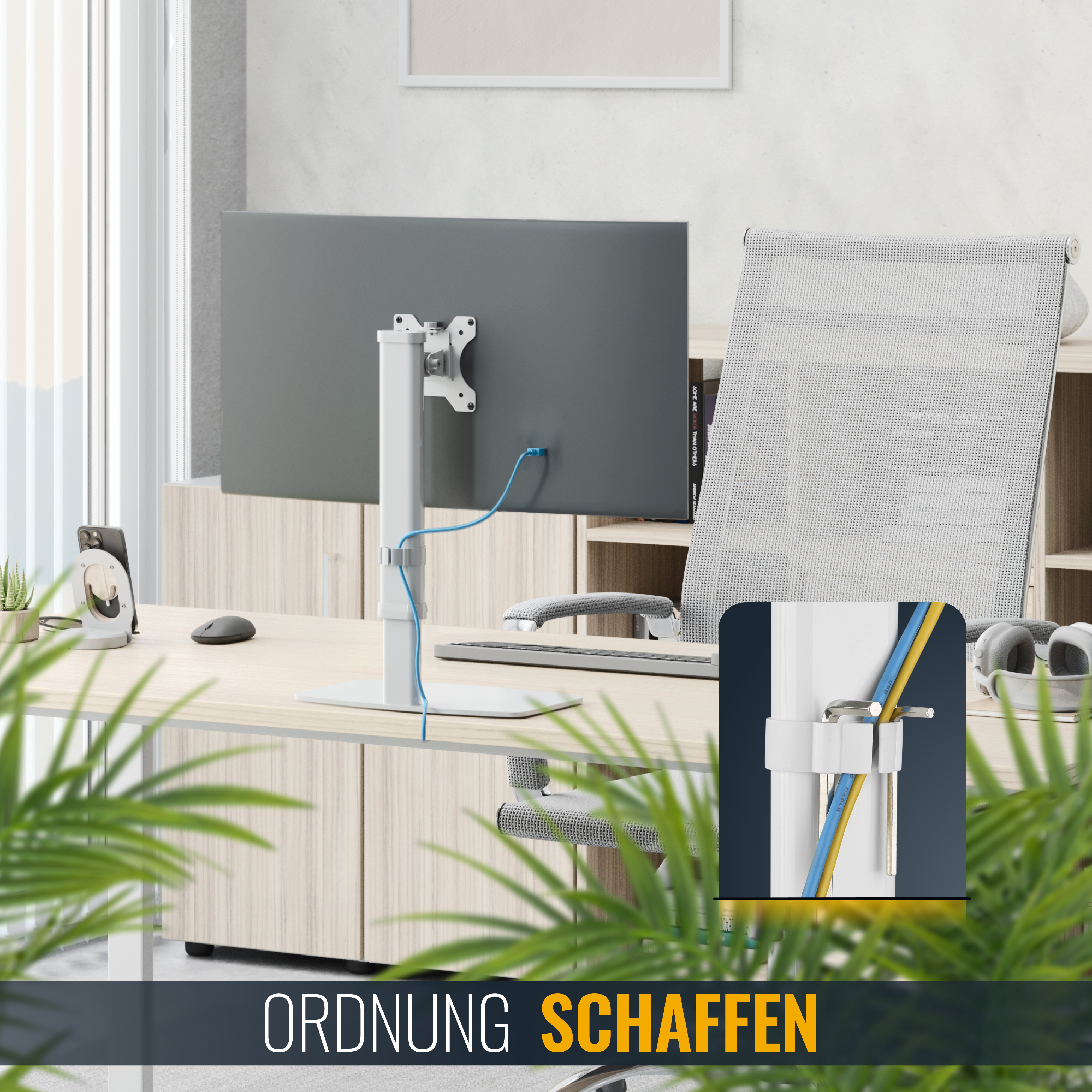 Ein Schreibtisch mit Monitor, Kabelmanagementsystem und grünen Pflanzen im Vordergrund.