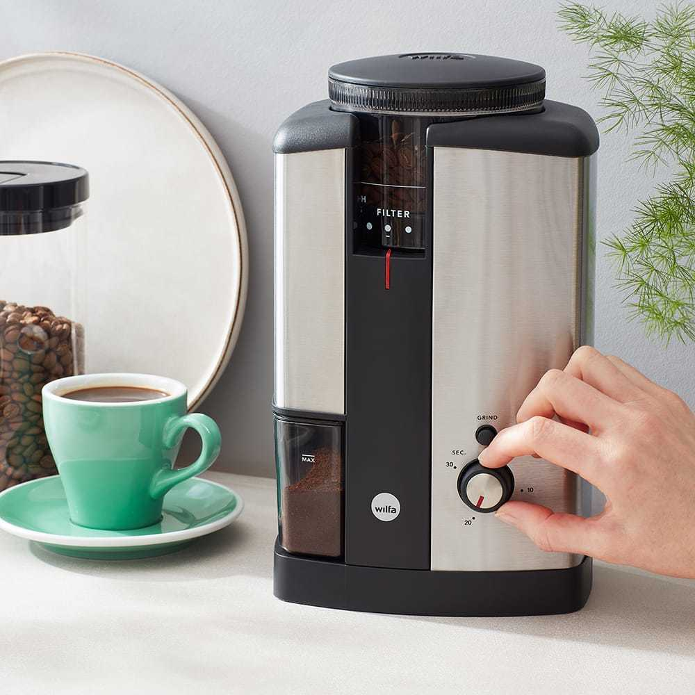 Kaffeemühle mit Bohnen und gemahlenem Kaffee sichtbar. Eine Hand dreht den Mahleinstellungsregler.