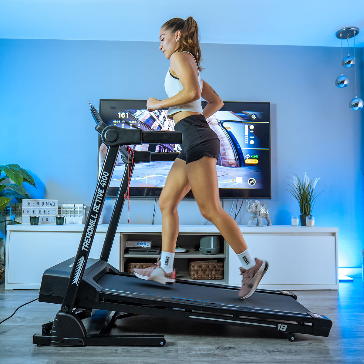 Mujer corriendo en una cinta, en una habitación con TV e iluminación azul.