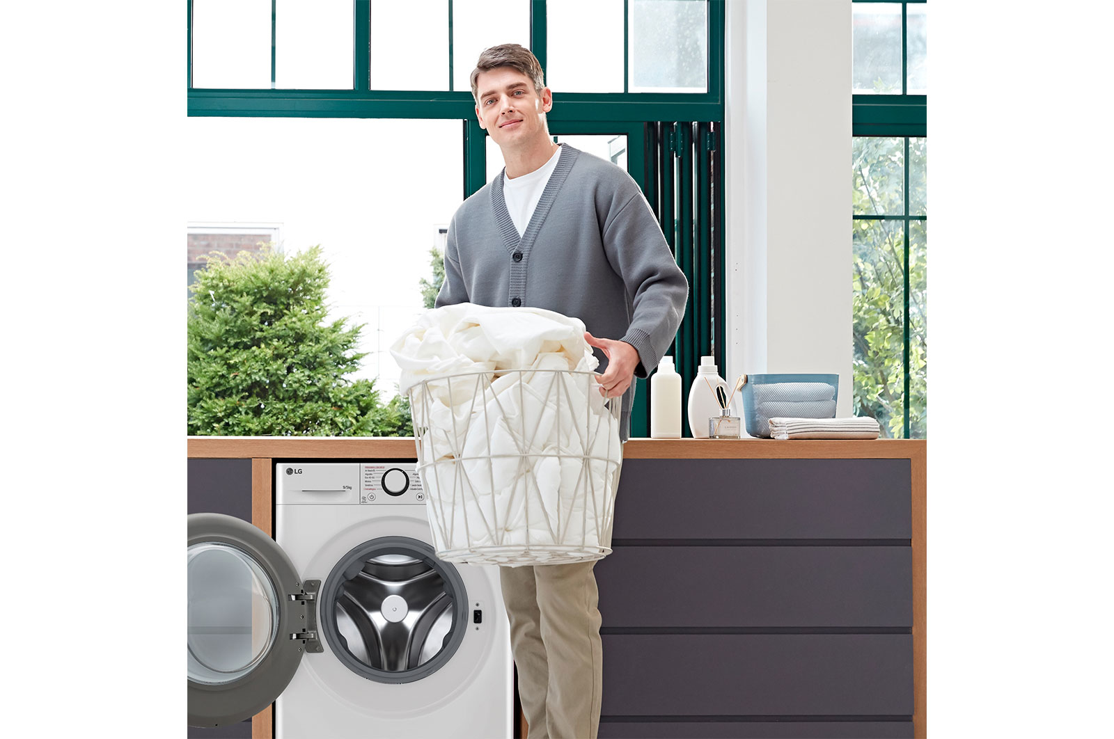 Mężczyzna trzymający kosz z praniem przed pralką LG.