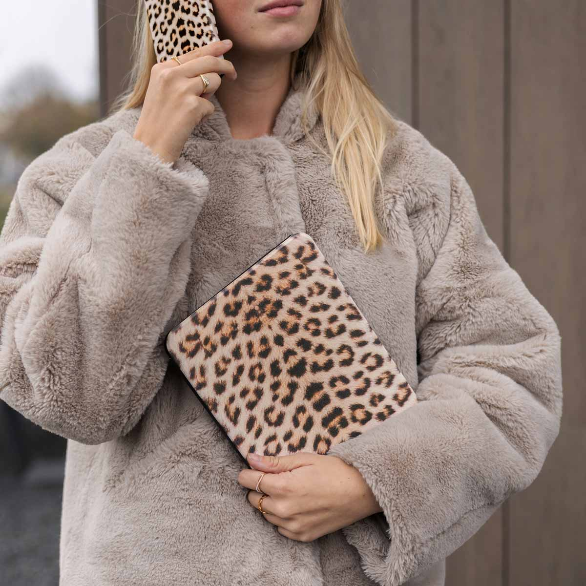 Woman holding a leopard print tablet and phone. She wears a fur coat.