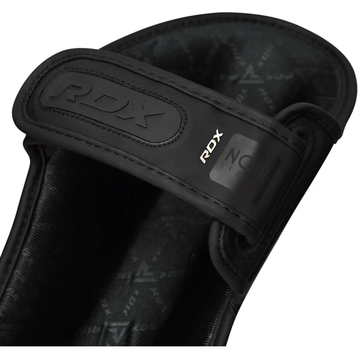 Nahaufnahme eines schwarzen RDX Noir Series Schienbeinschoners, mit Logo und Riemendetail.