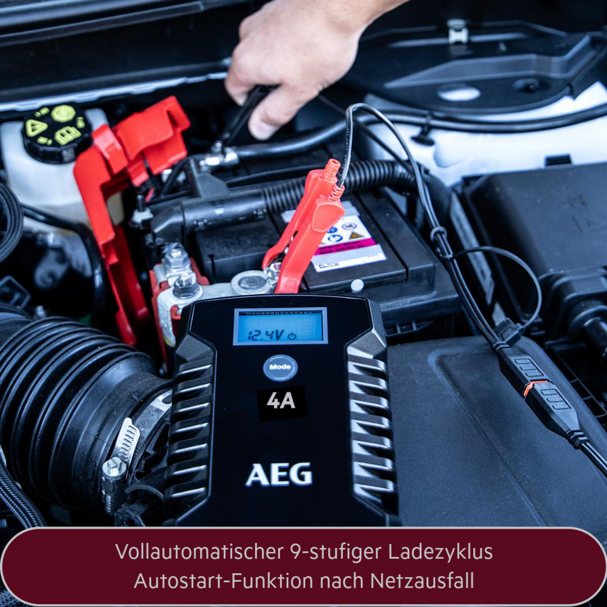 Autobatterieladegerät mit Display und Klemmen, im Motorraum eines Autos.