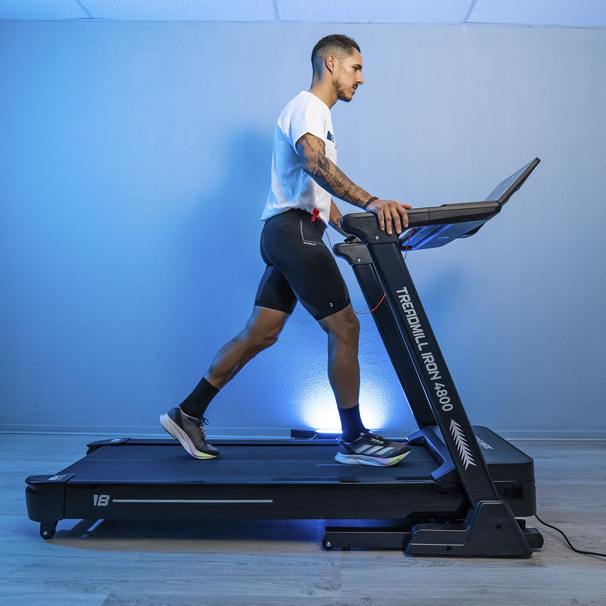 Hombre corriendo en una cinta de correr negra en una habitación con iluminación azul.