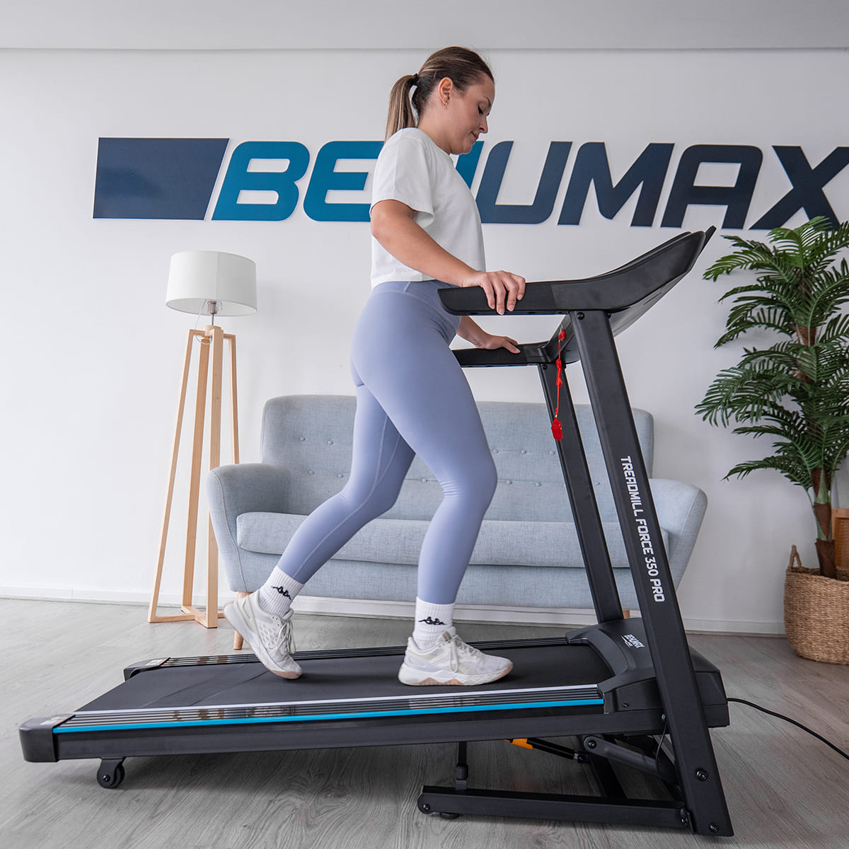 Una mujer camina en una cinta de correr. Al fondo un sofá y una lámpara.