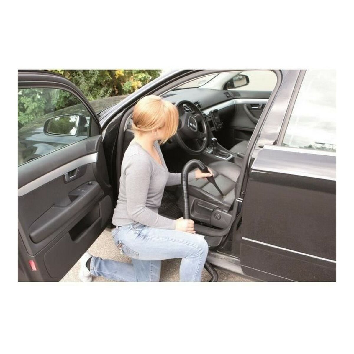 Woman cleaning car seat with a vacuum cleaner. The car door is open.