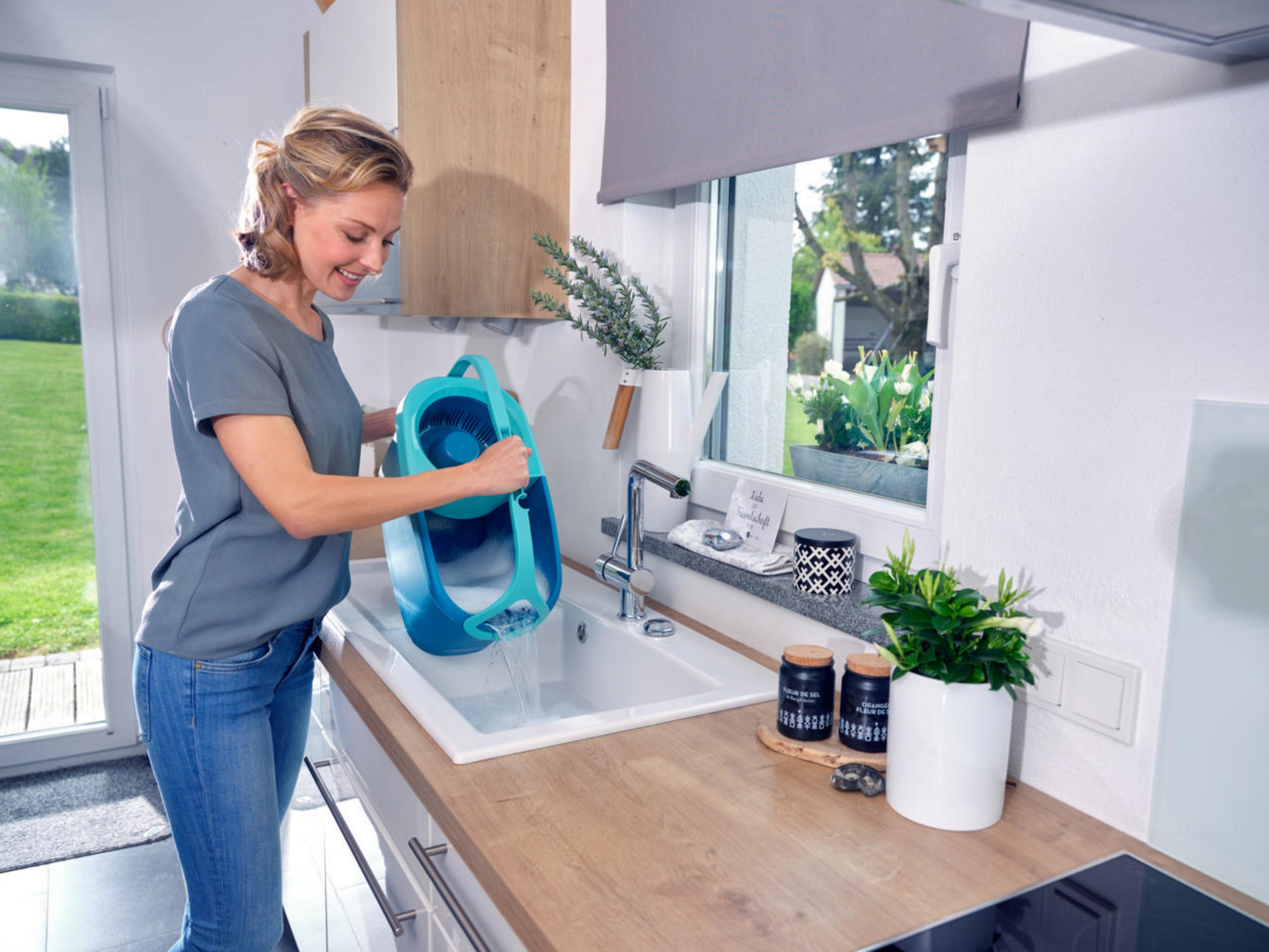 Kobieta wlewa wodę z niebiesko-białej konewki do zlewu.