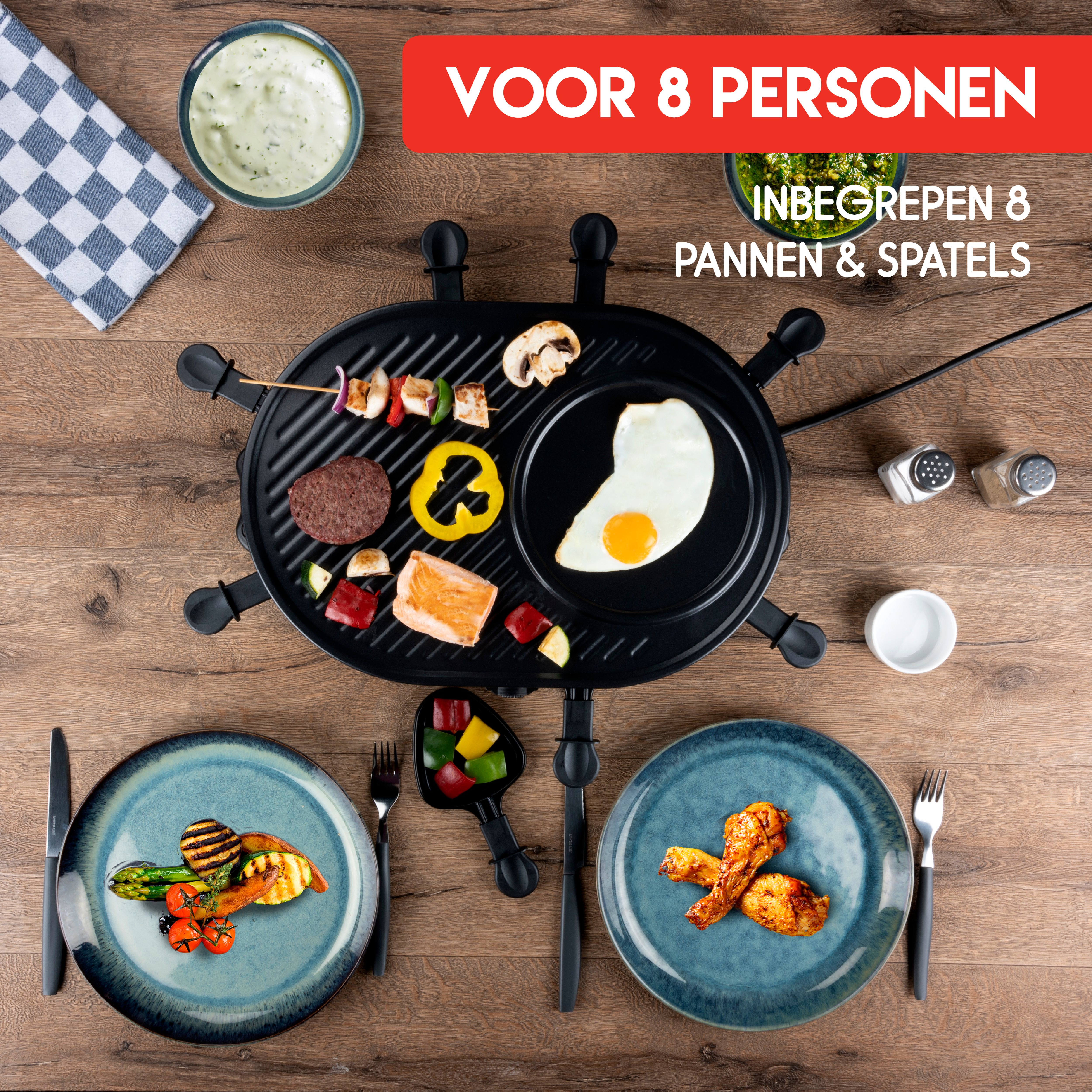 Draufsicht auf einen Raclette-Grill mit verschiedenen gekochten Speisen und Tellern, auf einem Holztisch.