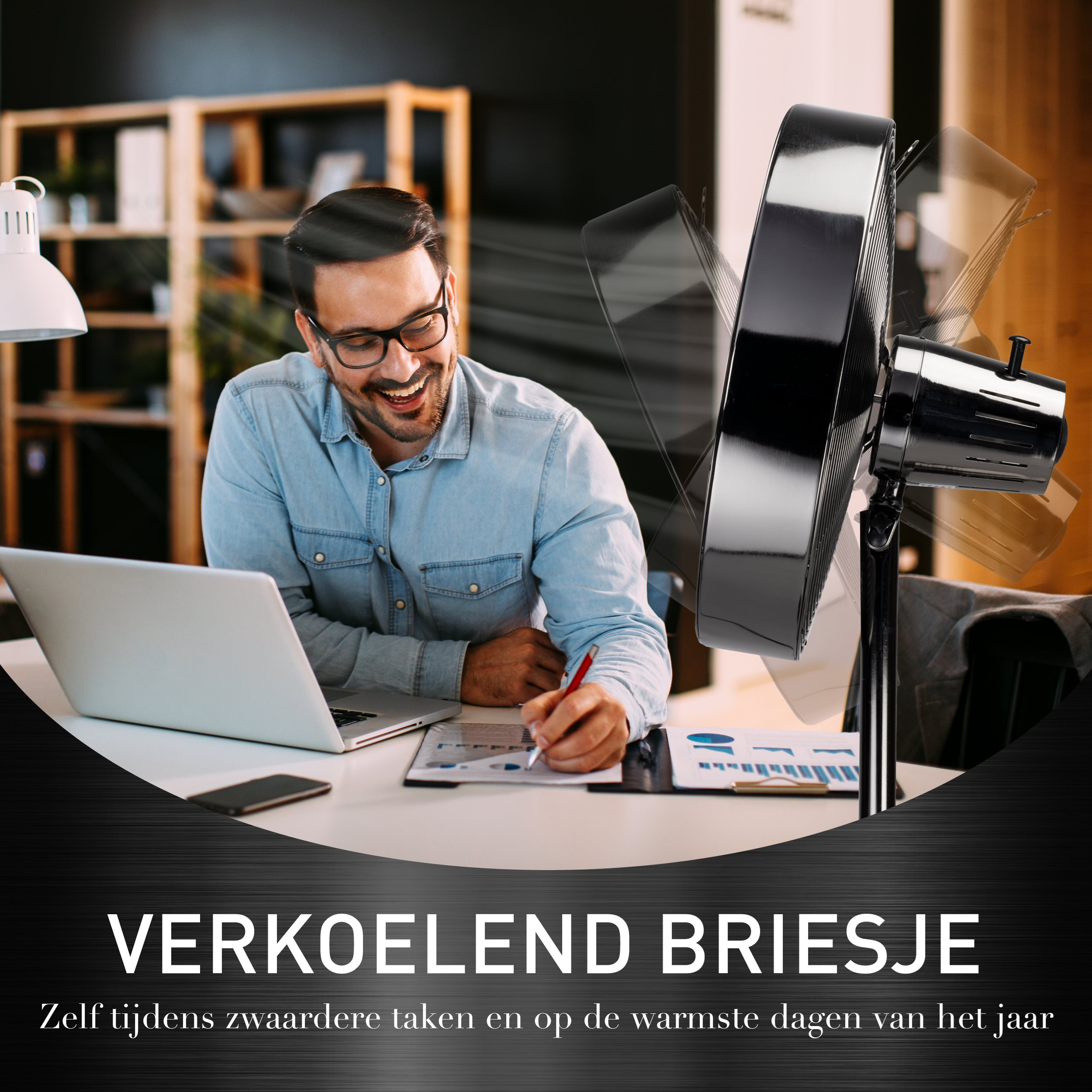 Man working at a desk with a laptop and a fan blowing air.