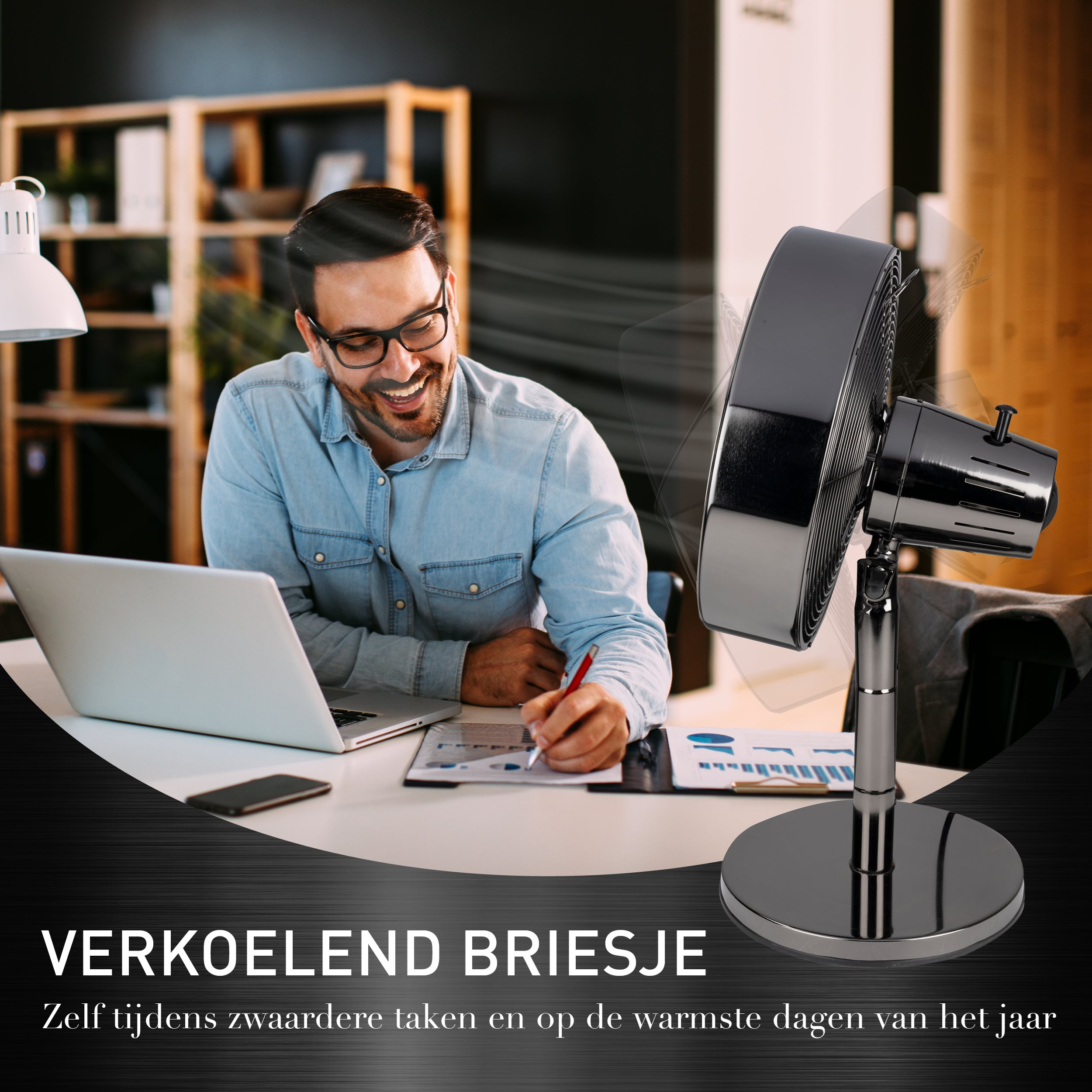Un homme souriant dans un bureau avec un ventilateur, un ordinateur portable et un document.