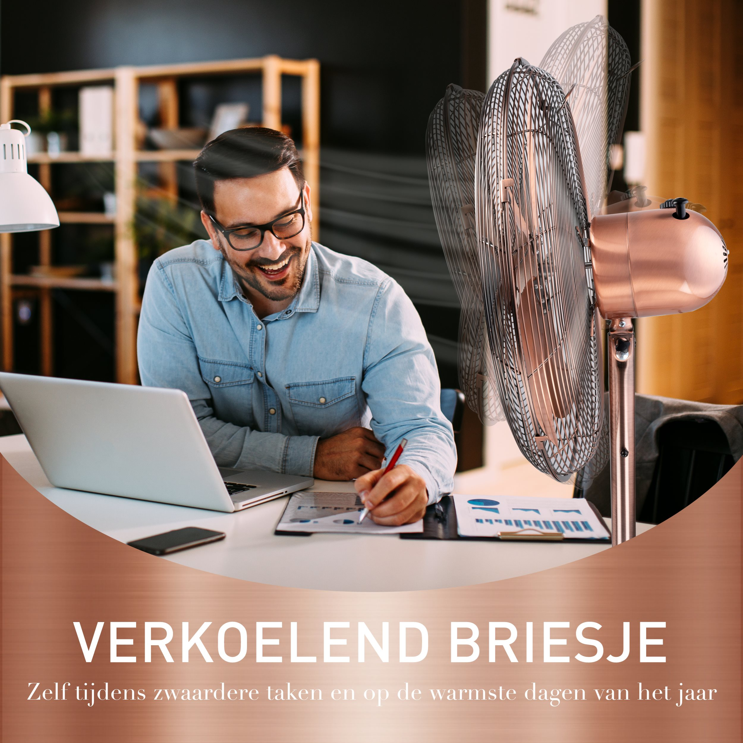 Homme avec des lunettes sourit à un ordinateur portable. Un ventilateur souffle de l'air. Le fond est un bureau à domicile.