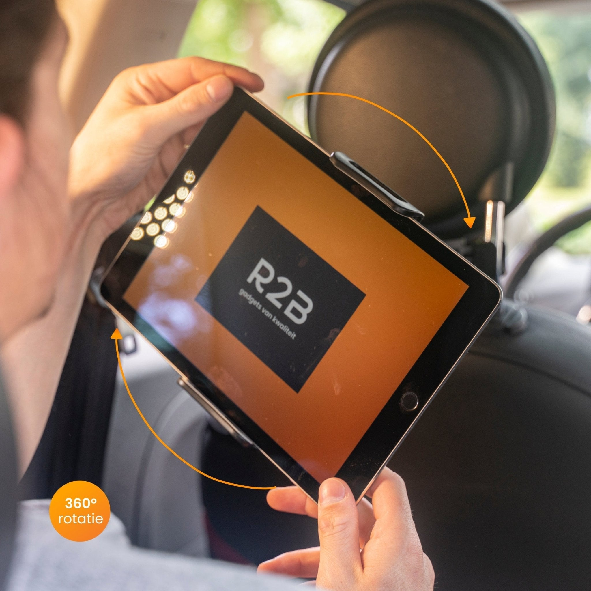 Eine Person hält ein Tablet in einem Auto, das an einer Kopfstütze befestigt ist. Tablet zeigt einen orangefarbenen Bildschirm und Logo.