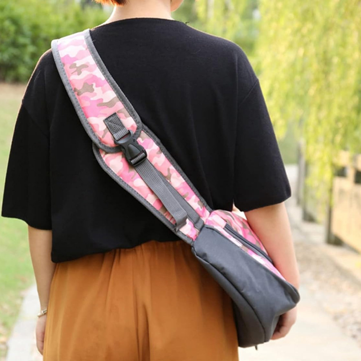 Person trägt ein schwarzes Hemd und eine braune Hose. Eine rosa Tarnung Tasche ist über der Schulter.