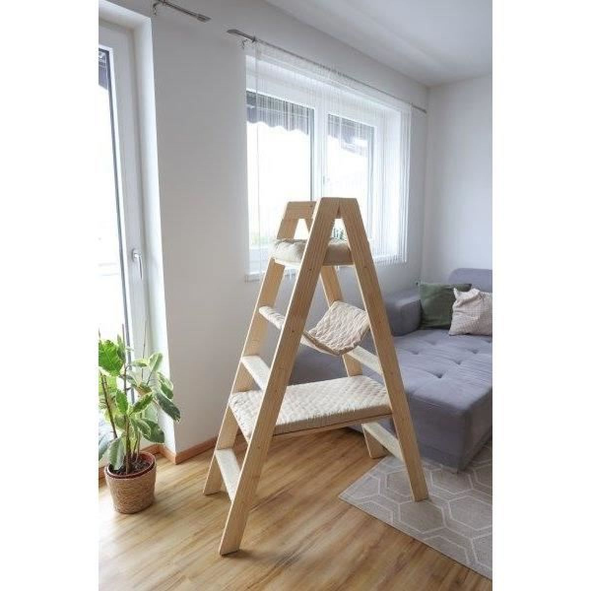Katzenmöbel aus Holz mit mehreren Plattformen. In einem Raum mit Fenster und Sofa.