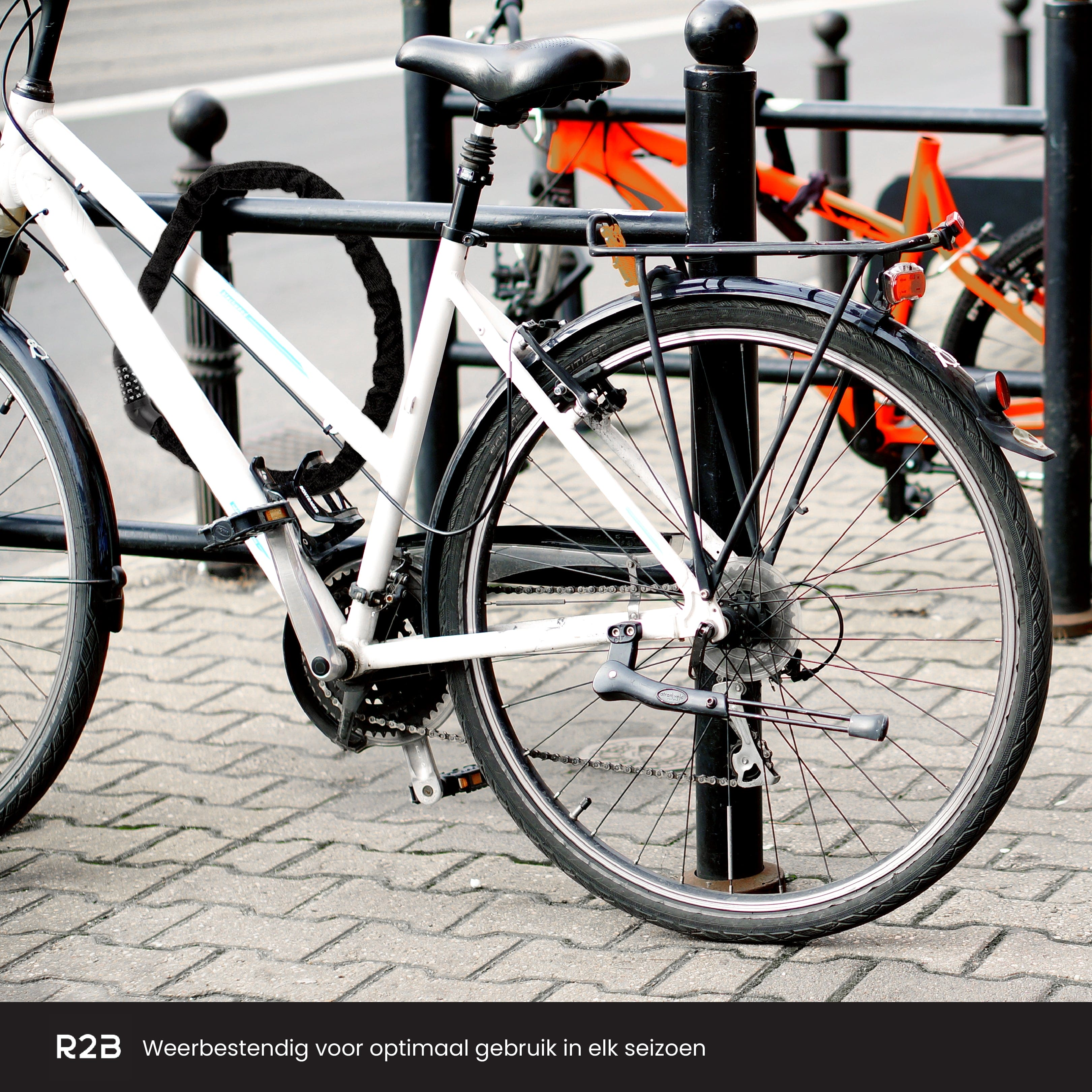 Weißes Fahrrad an einem schwarzen Zaun angeschlossen. Ein weiteres Fahrrad im Hintergrund. Gepflasterter Boden.