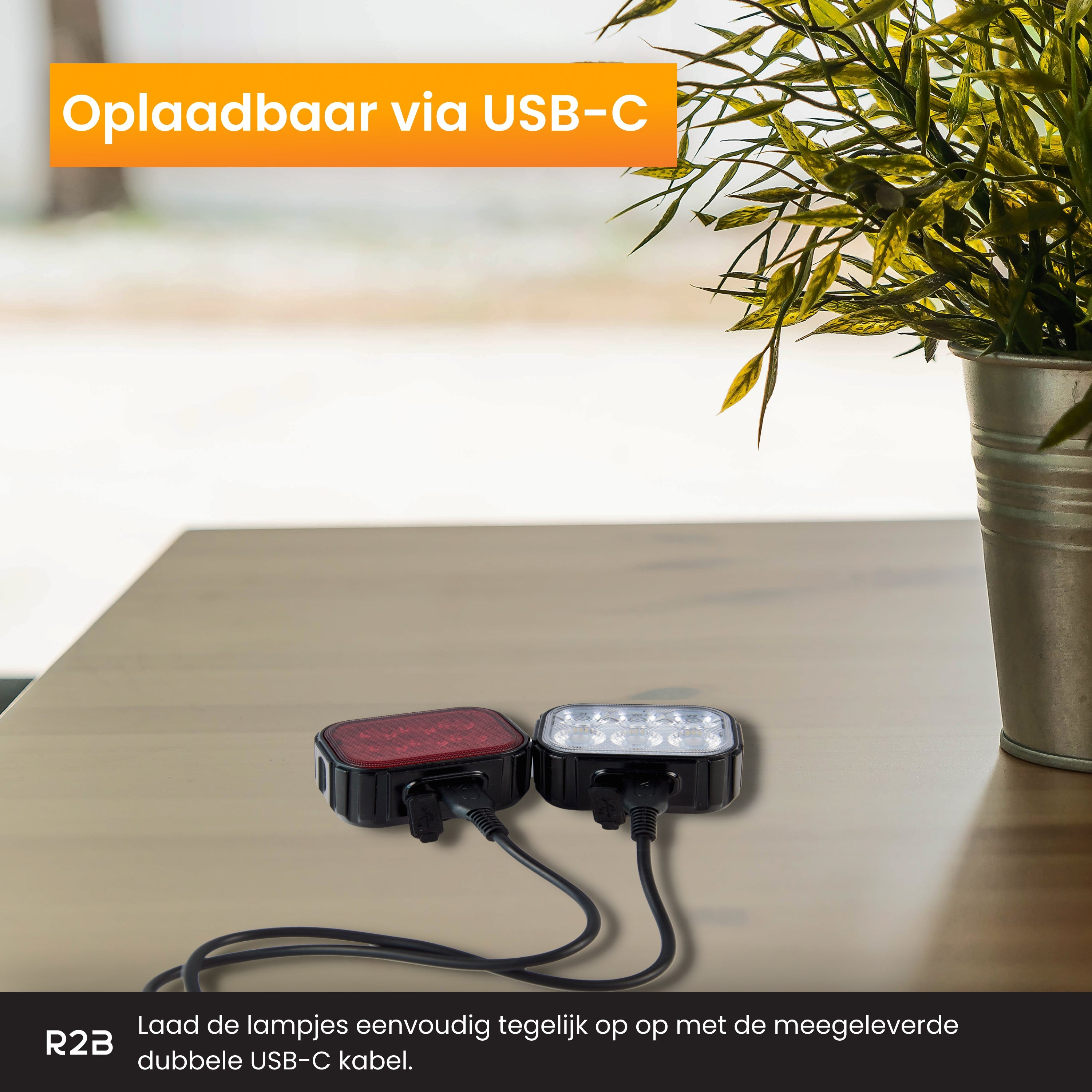 Two bike lights, one red, one white, connected by a USB-C cable, on a wooden table.