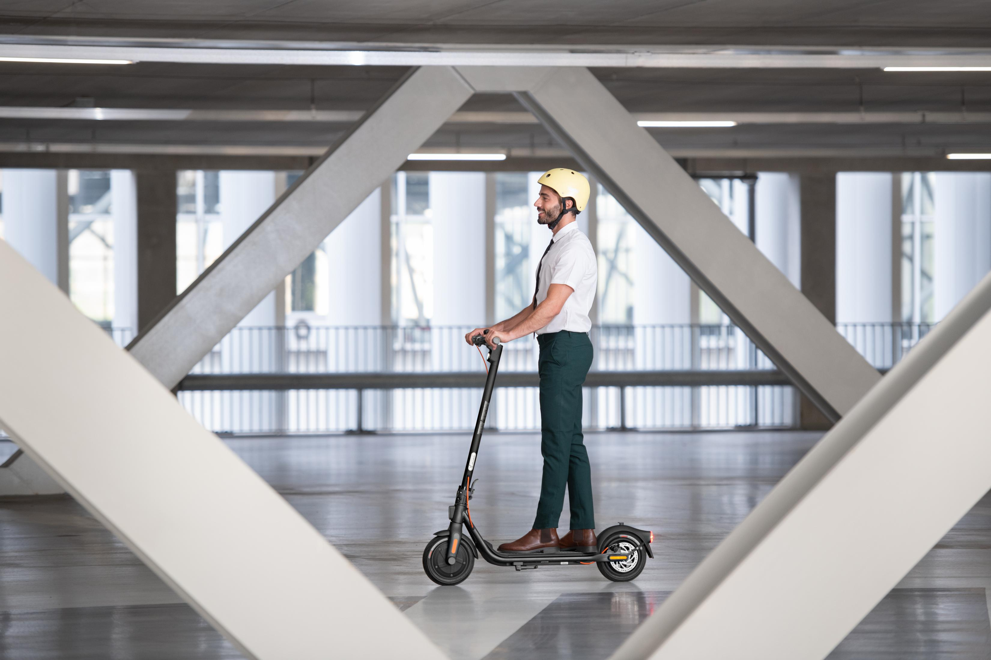 Mann mit Helm fährt E-Roller in einer Parkgarage. Der Hintergrund zeigt geometrische Betonstrukturen.