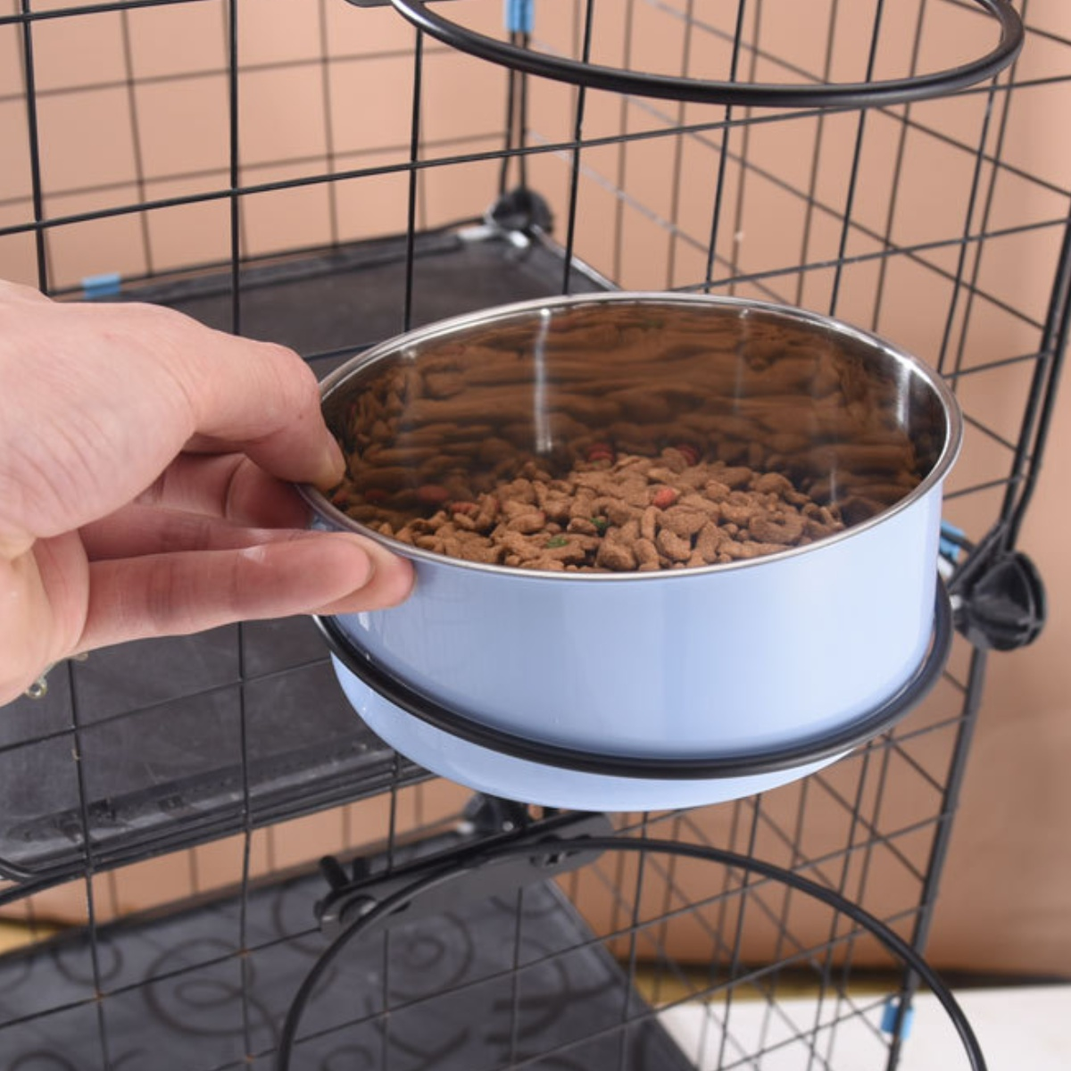 Eine Hand hält eine hellblaue Katzennapf mit braunen Trockenfutter gefüllt, in einem Katzenkäfig.