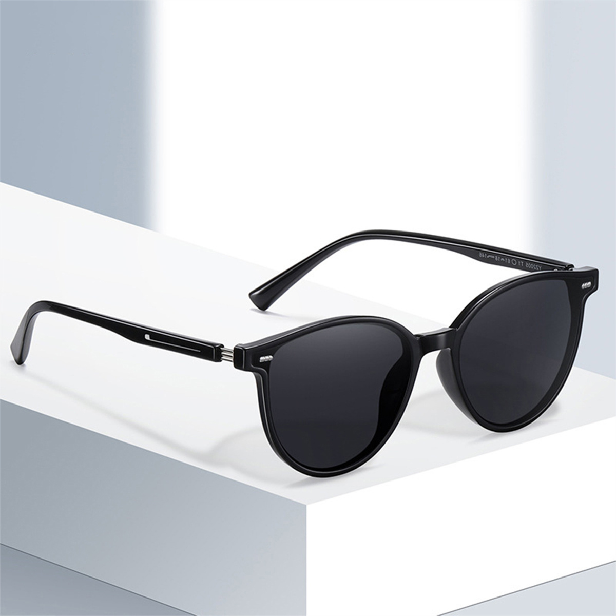 Schwarze Sonnenbrille mit rundem Rahmen. Sie sind vor einem neutralen Hintergrund platziert.