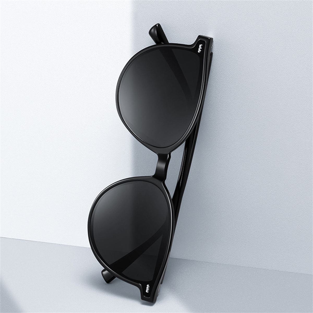 Schwarze Sonnenbrille lehnt an einer weißen Wand. Die Sonnenbrille ist rund.