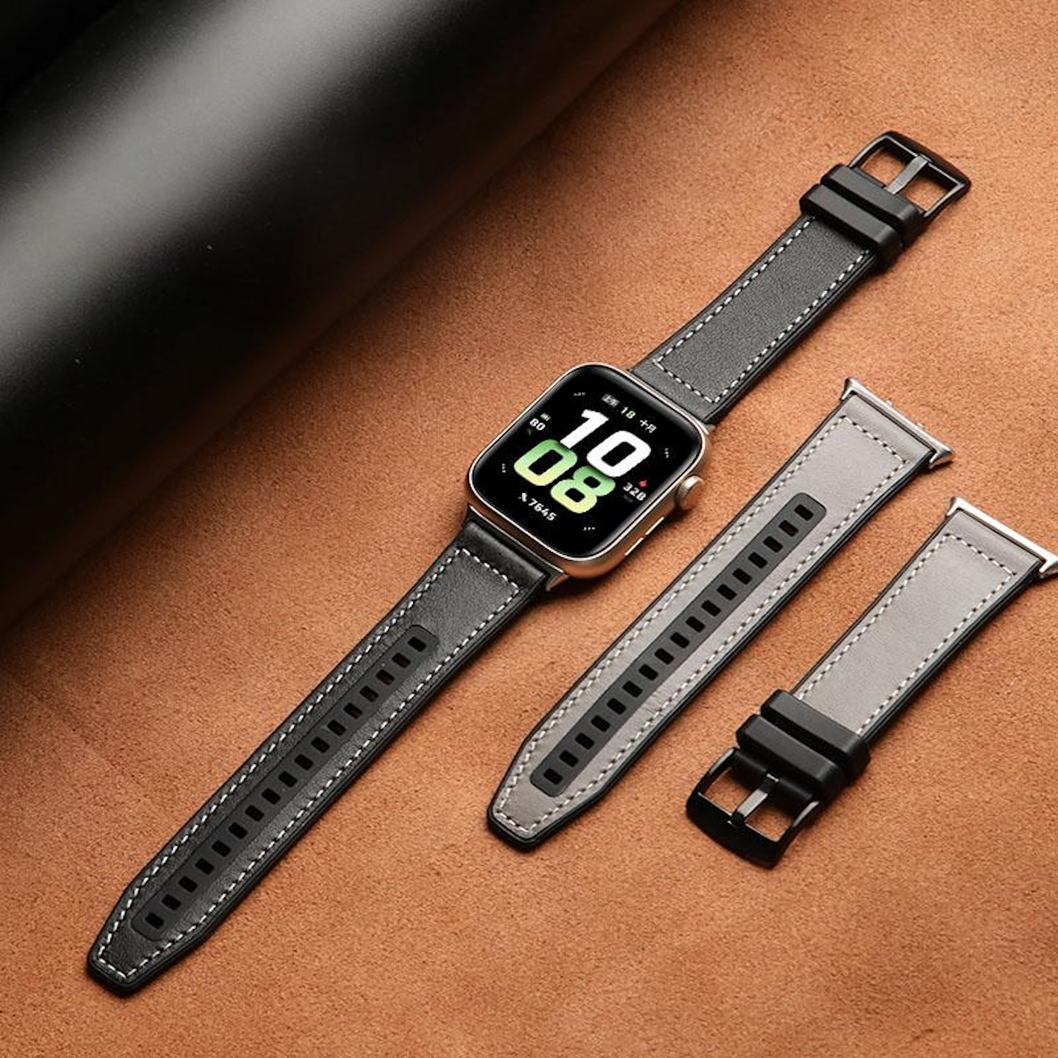 Eine Smartwatch an einem Lederarmband, mit einem Ersatzarmband daneben, alles auf brauner Lederoberfläche.