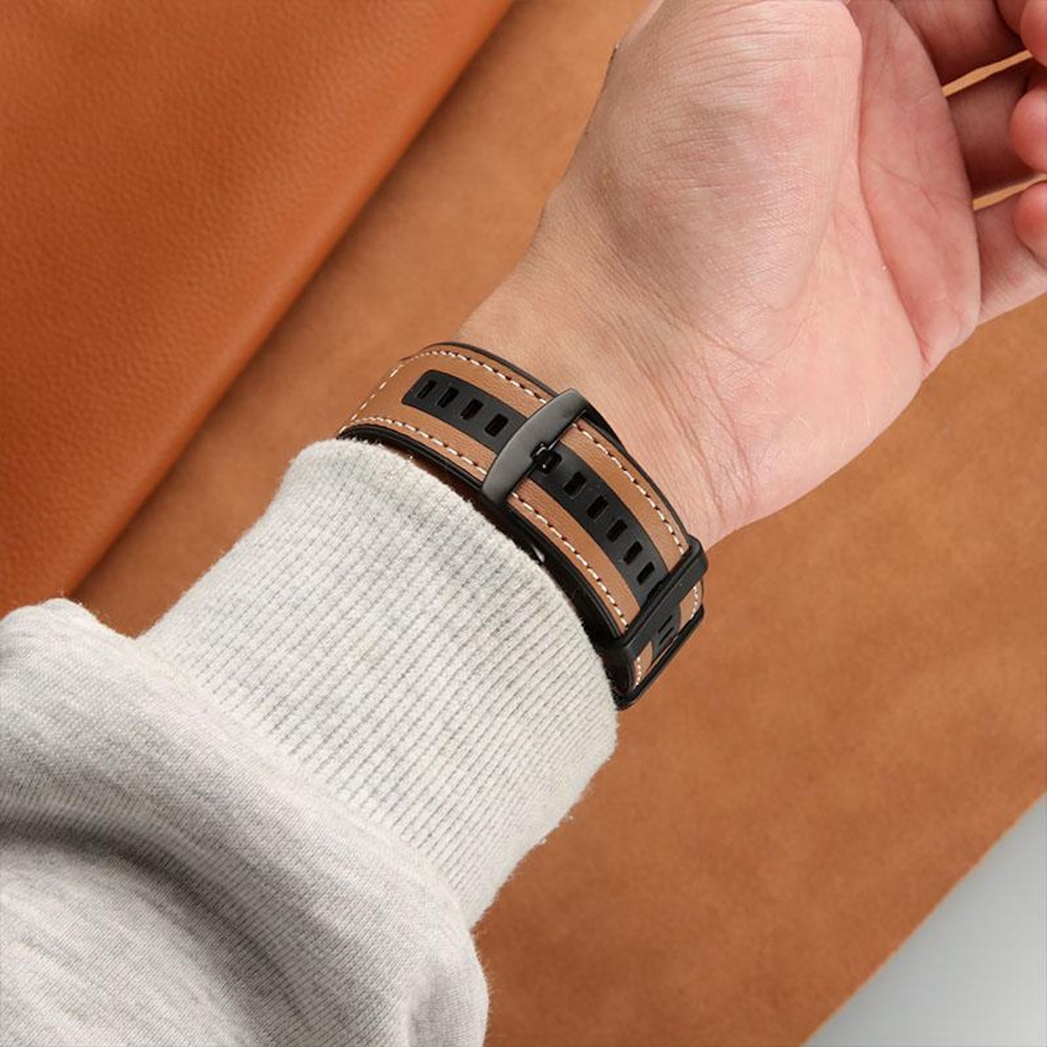 Das Handgelenk einer Person mit einer Uhr, mit einem schwarzen und braunen Armband, über einer braunen Oberfläche.