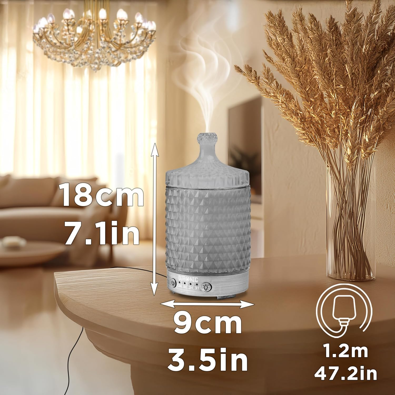 Grauer Aroma-Diffusor mit Abmessungen, eine Vase mit Weizen und ein Kronleuchter im Hintergrund.