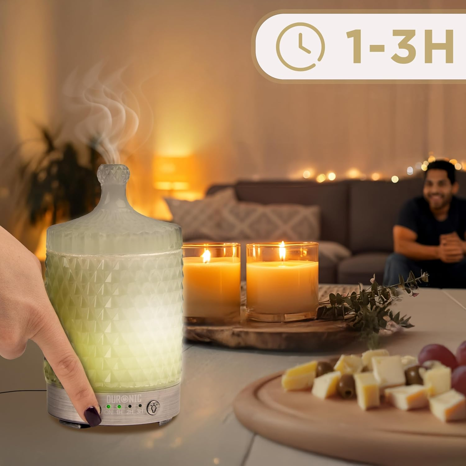 Eine Hand berührt einen Diffusor. Kerzen und Essen stehen auf einem Tisch. Ein Mann sitzt im Hintergrund.