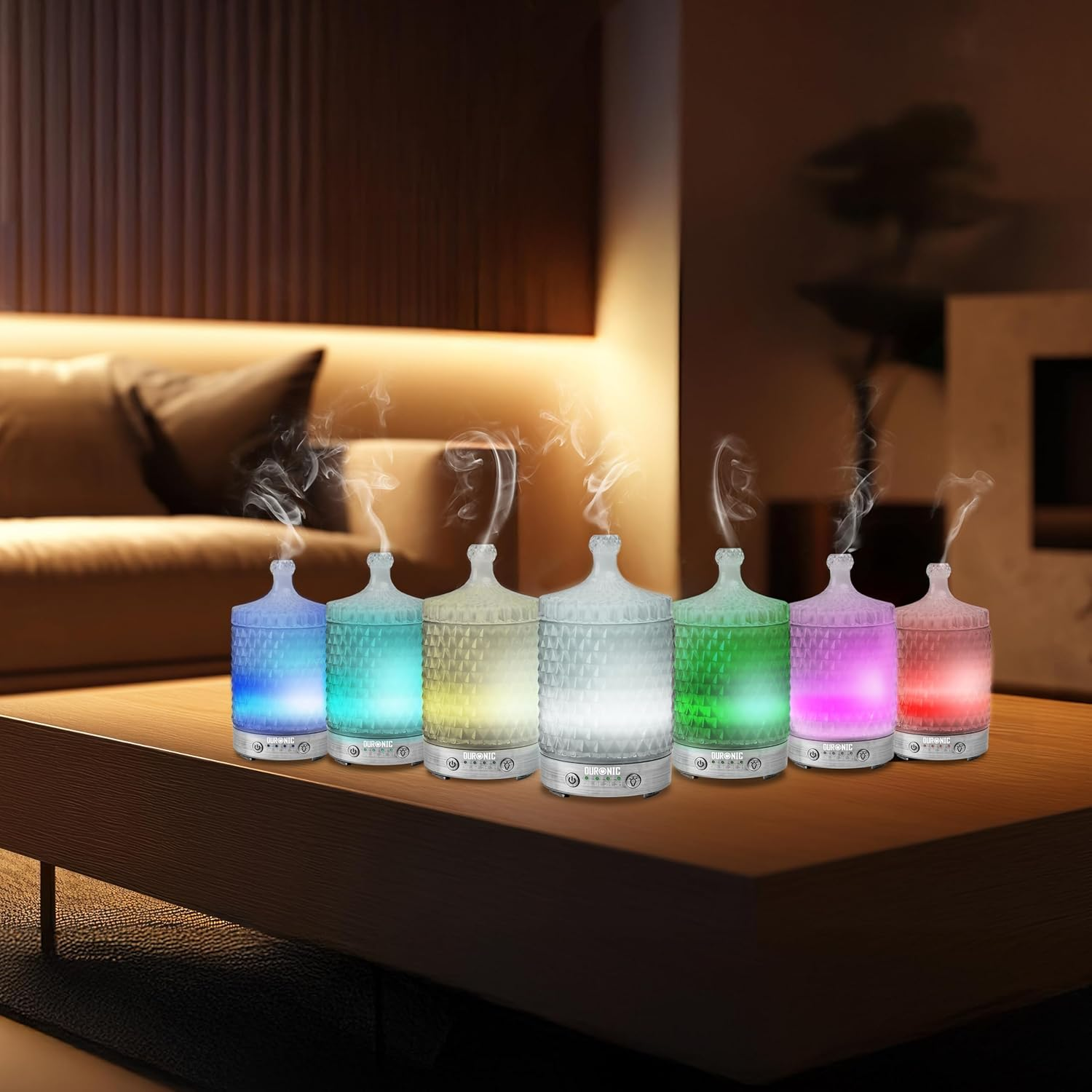 Reihe beleuchteter Aromadiffusoren, die Dampf abgeben, verschiedene Farben, auf einem Holztisch.