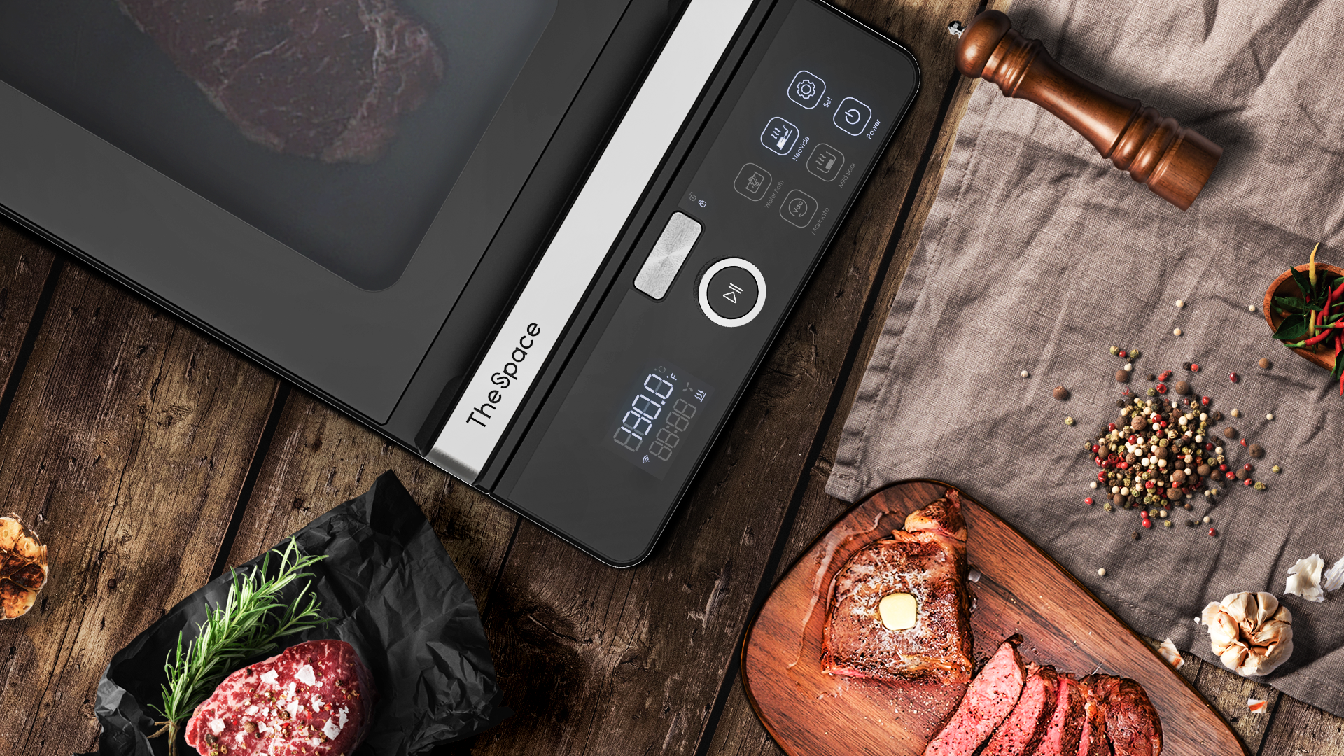 Cucina sous vide nera con display. Bistecca, aglio e pepe intorno.