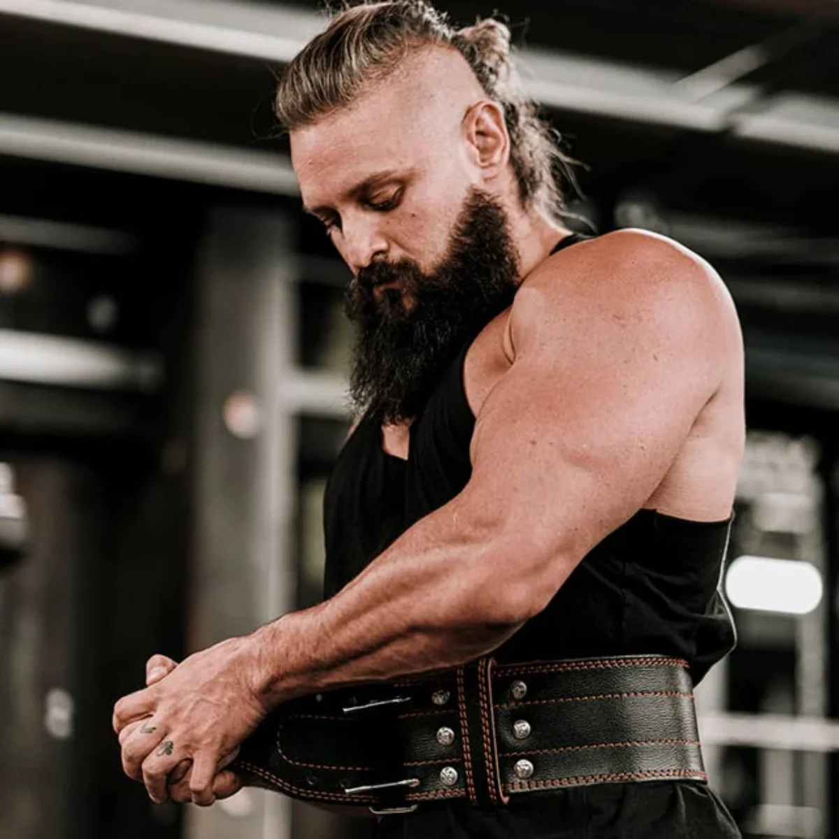 A man in a gym wearing a weightlifting belt. He has a beard and a sleeveless shirt.