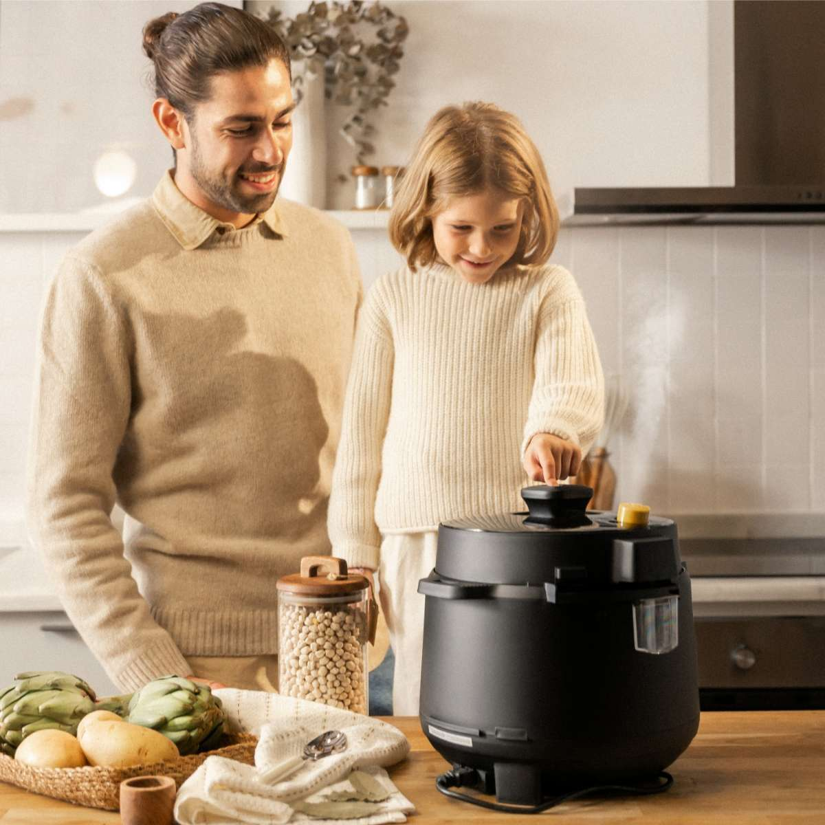 Un hombre y una niña en la cocina. Hay una olla negra en la mesa. Verduras en la mesa.