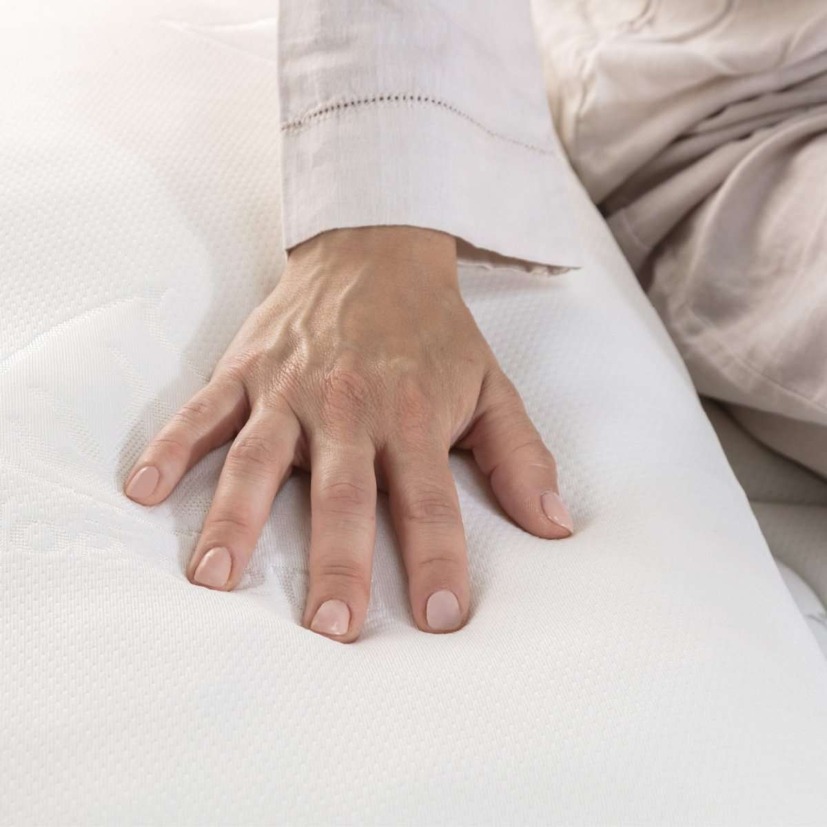 La mano de una persona toca suavemente un colchón blanco. La mano está enfocada.