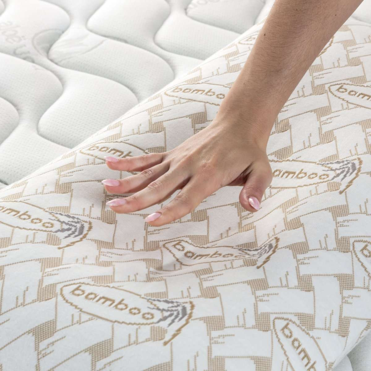 Una mano tocando una almohada en una cama. La almohada tiene diseño de bambú y la cama es blanca.