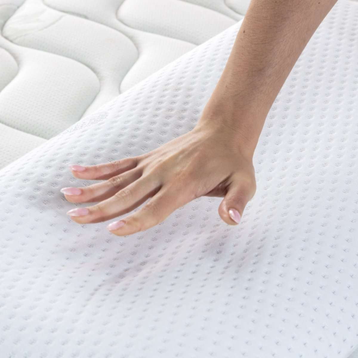 Una mano presiona suavemente sobre un colchón blanco, mostrando su textura y suavidad.