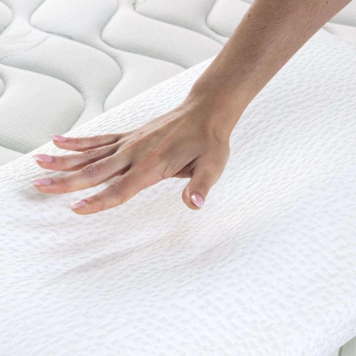 Una mano tocando una almohada blanca sobre un colchón blanco.