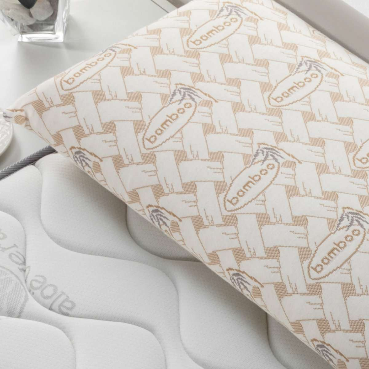 Almohada con un patrón de bambú, sobre un colchón blanco. La almohada tiene el texto 'bamboo'.