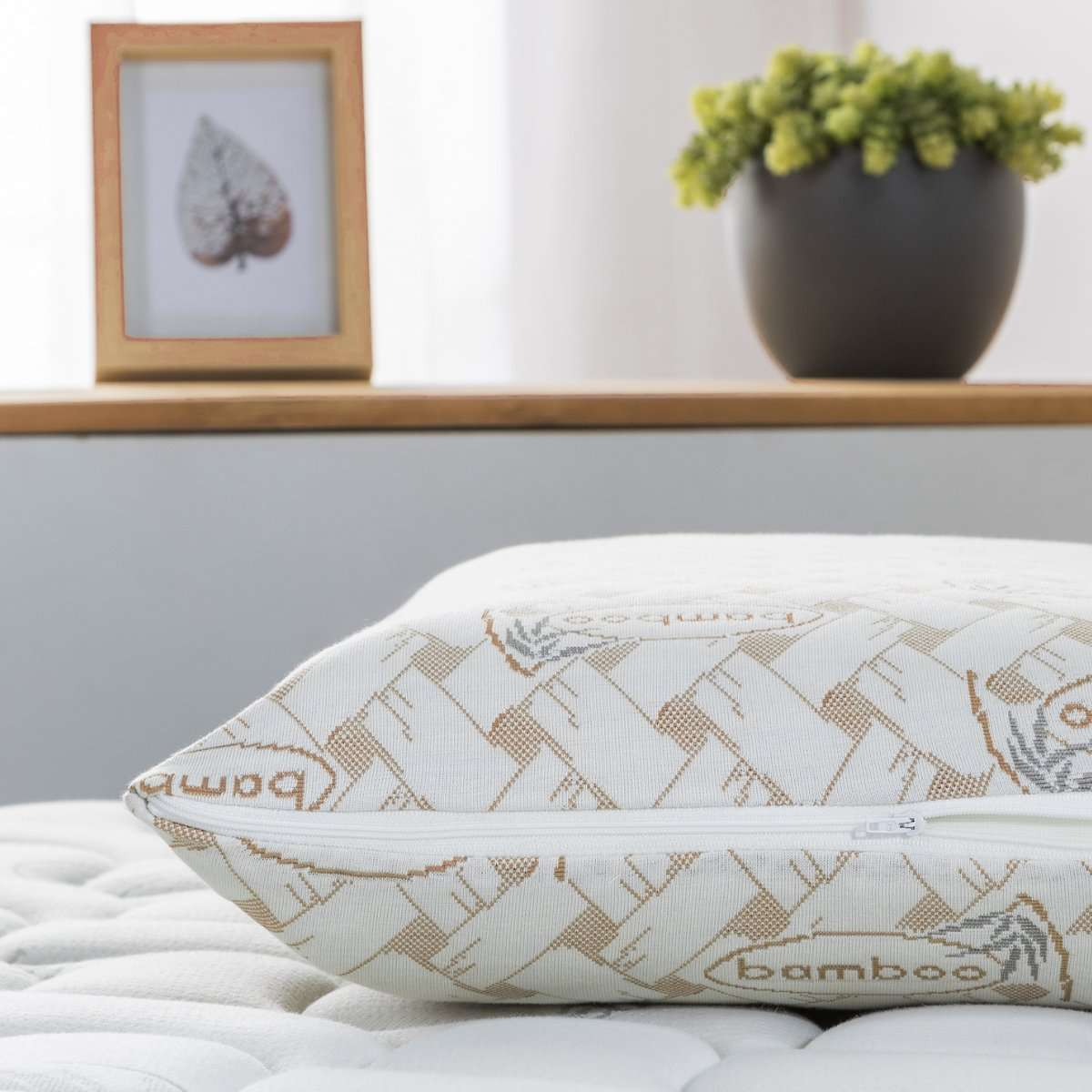Una almohada de bambú con cremallera, sobre un colchón blanco, junto a la decoración.