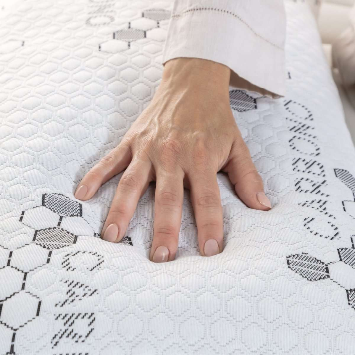Una mano presiona un colchón blanco con un patrón hexagonal, creando una hendidura.