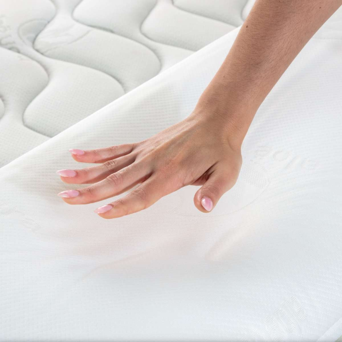 Una mano toca la superficie de un colchón blanco. El colchón tiene un patrón acolchado.