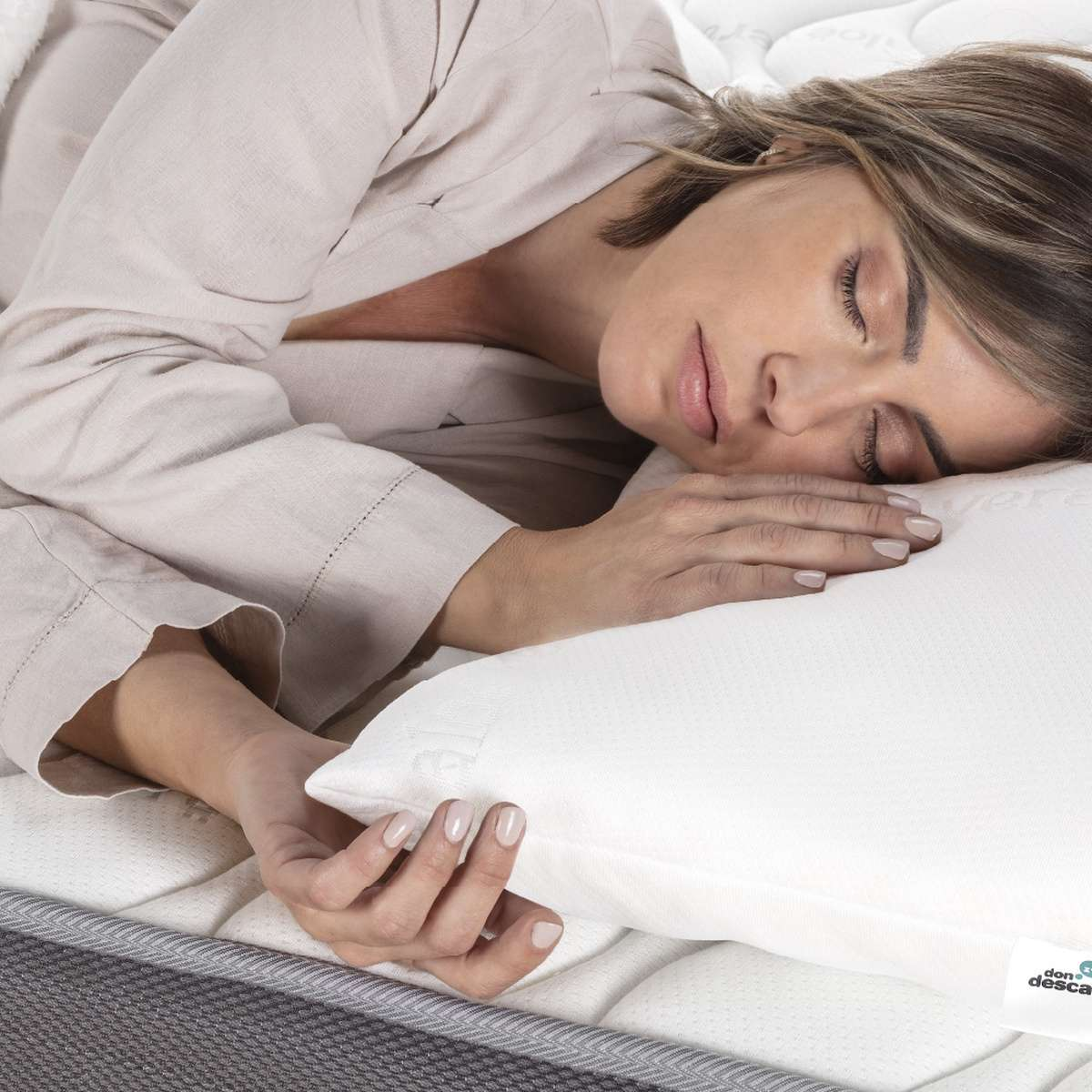 Una mujer durmiendo sobre un colchón, apoyando su cabeza en una almohada blanca.