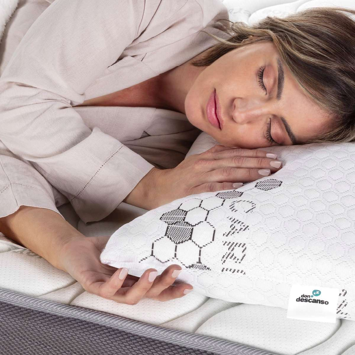 Mujer durmiendo en una cama con una almohada. La almohada tiene un logo. La mujer lleva una bata.