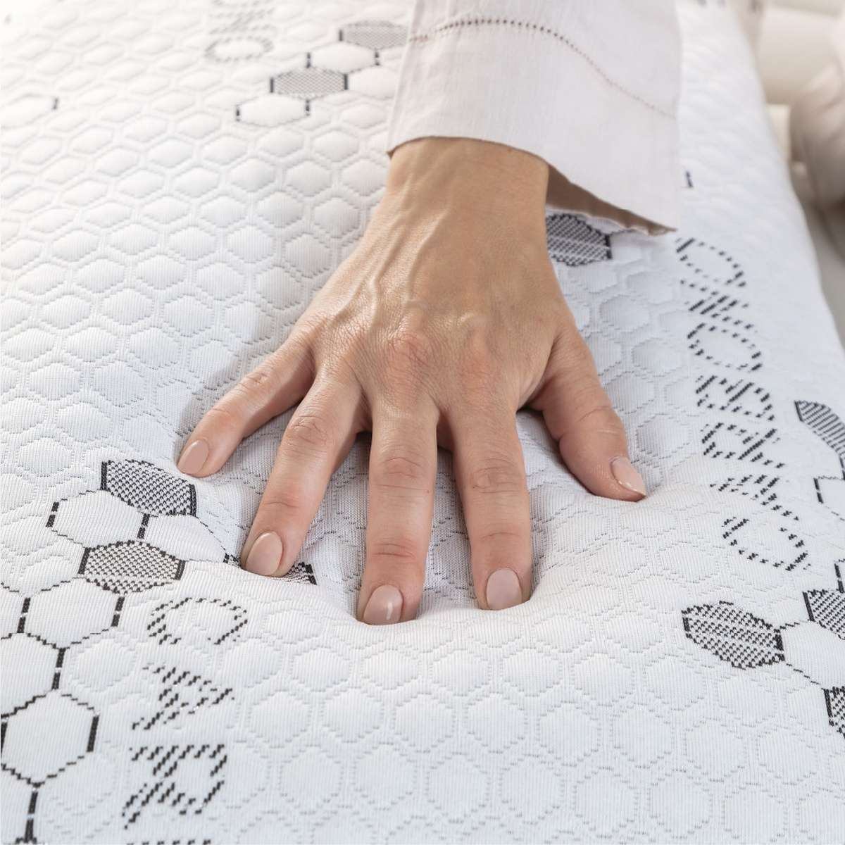 Una mano presionando sobre un colchón blanco con patrón de panal.