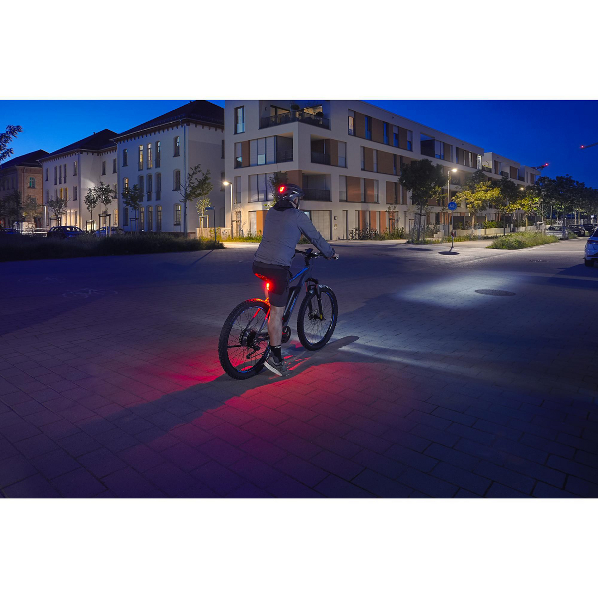Ein Radfahrer mit Lichtern an seinem Fahrrad fährt nachts. Gebäude und Straße sind im Hintergrund.