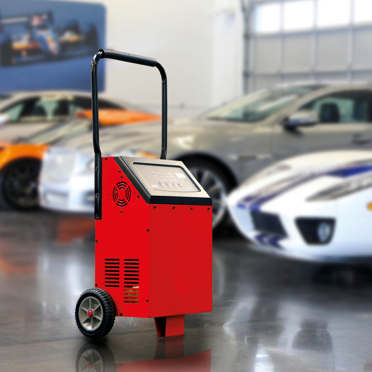 Rotes und schwarzes Ladegerät auf Rädern in einer Garage. Autos sind im Hintergrund verschwommen.