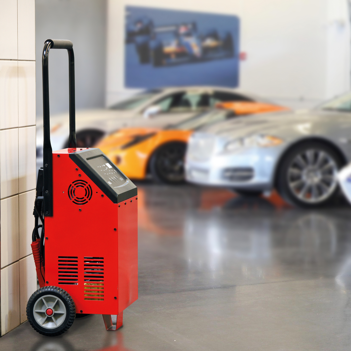 Rotes Autoladegerät auf Rädern, in einer Garage mit verschwommenen Autos im Hintergrund.