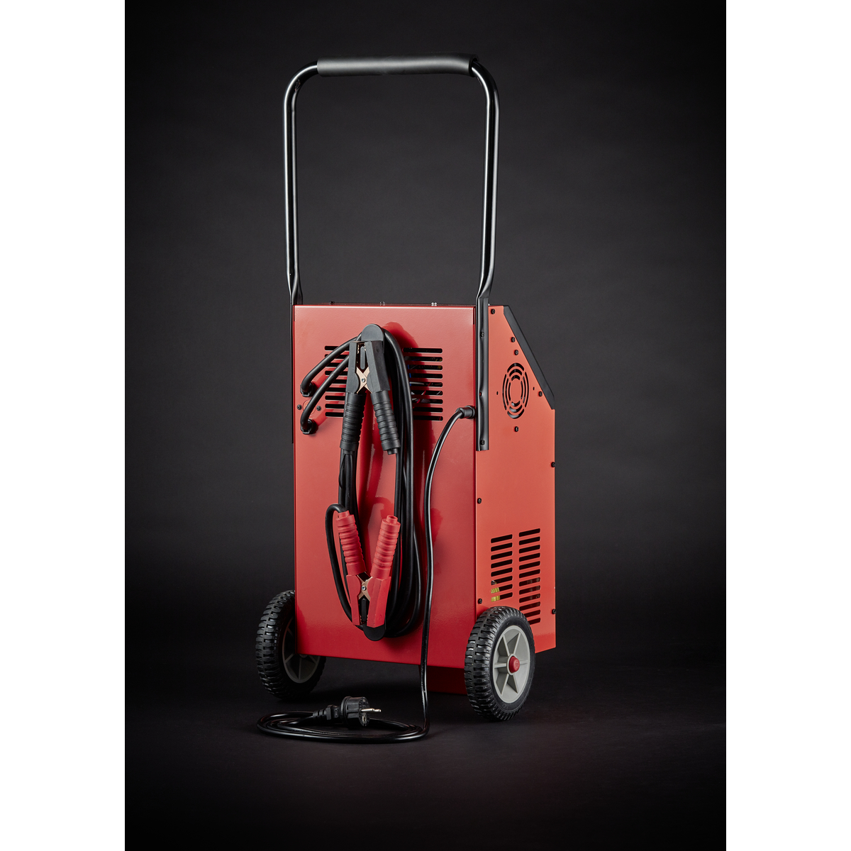 Rotes Batterieladegerät auf Rädern mit schwarz-roten Kabeln und schwarzem Hintergrund.