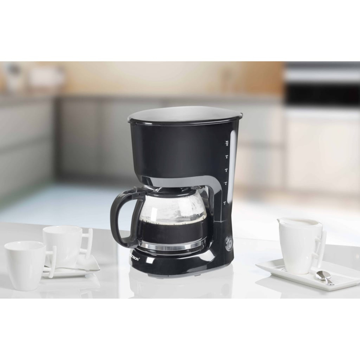 Caffettiera nera, caraffa in vetro, tazze bianche su un bancone. Sfondo cucina.